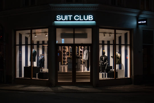 Facade af SUIT CLUB-butikken i Aarhus fotograferet om aftenen med oplyste udstillingsvinduer.